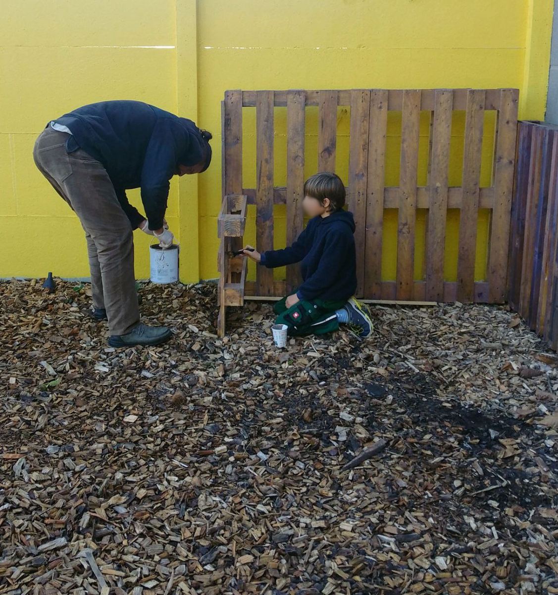 Un adulte et un enfant peignent un aménagement en bois dans la cour de l’école